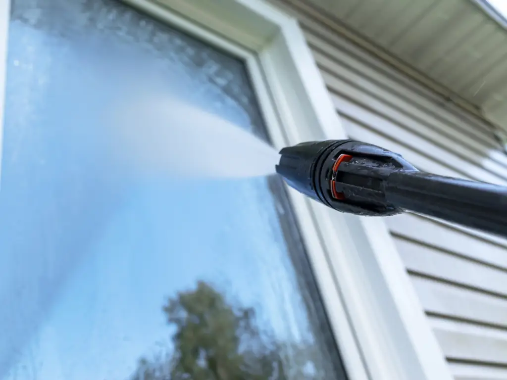Close-up pressure washing of a residential window on a Mount Laurel, NJ home — removing hard water staining, algae, and oxidation buildup from exterior window frames and glass.