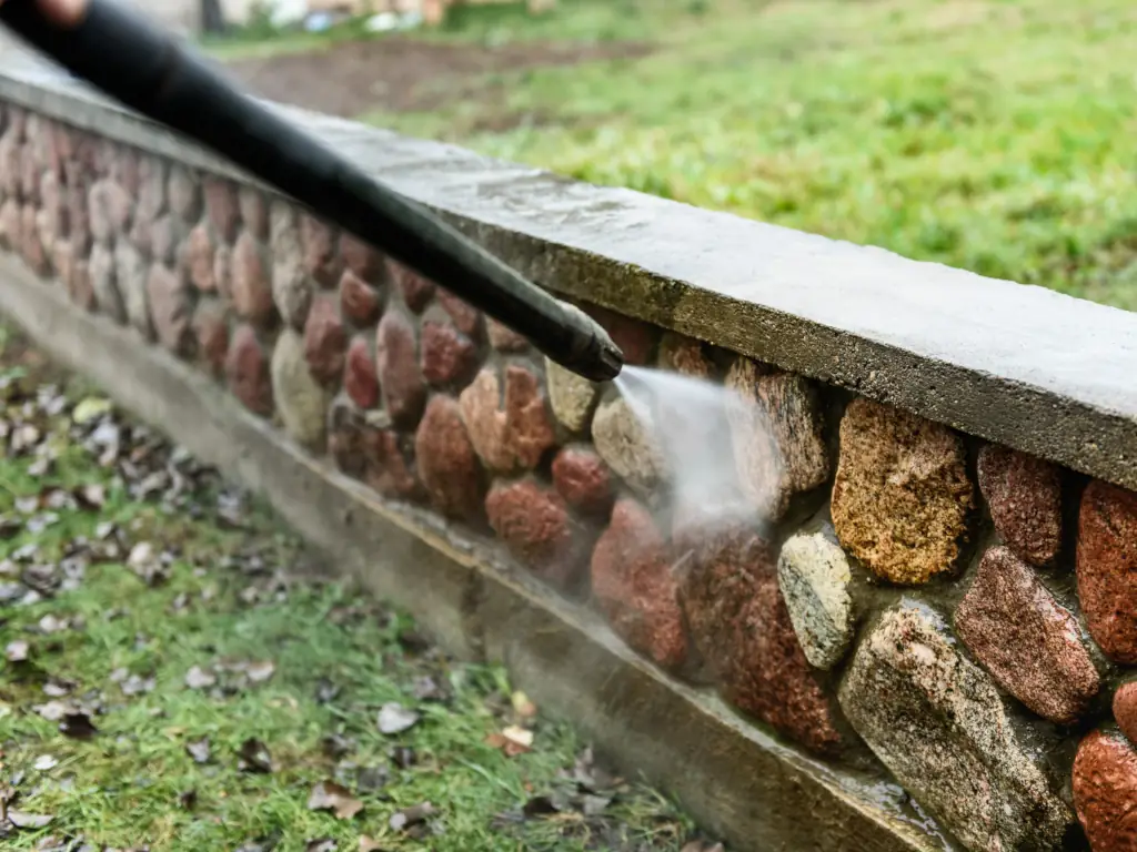 High-pressure power washing removing dirt and algae from a stone retaining wall on a Williamstown, NJ property — restoring the surface of backyard hardscape and garden walls.
