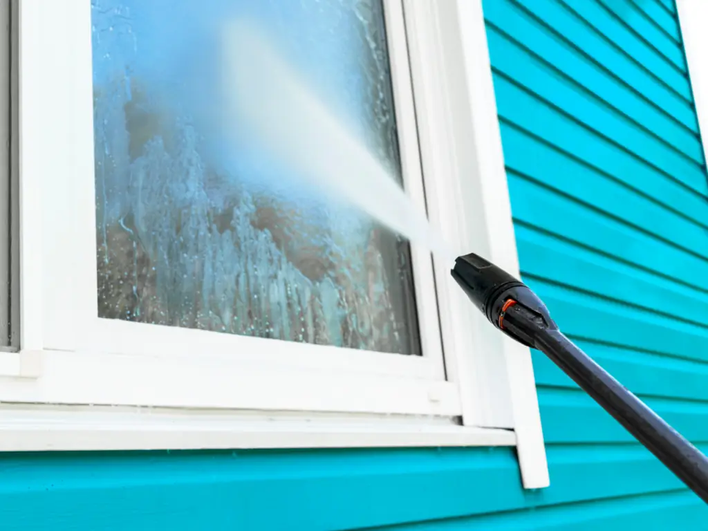 Power washing a window and vinyl siding on a Collingswood, NJ home — removing algae streaks, dirt, and mineral deposits from window frames, sills, and exterior siding.